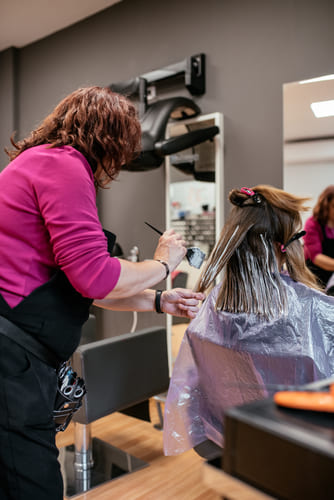 A hairdresser in a unisex salon in Kolkata is applying hair color to a client's hair.