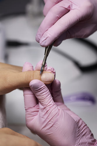 a nail care session at a unisex salon in Kolkata, showing a professional in pink gloves trimming cuticles with precision tools during a manicure treatment.