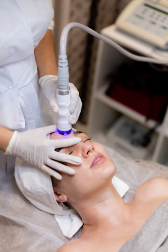 A woman getting a professional facial treatment with advanced skincare equipment at a unisex salon in Kolkata.